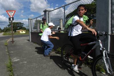 A teenaged boy keeps watch as his friends try to get the attention of some girls in the schoolyard.