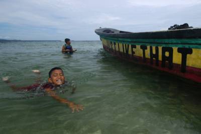 After using a boat as a diving platform, this boy swims back to the front to jump again.