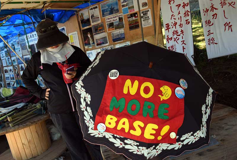 An activist with a parasol decorated with her feelings against plans to fill in a portion of Oura Bay for landing strips outside Camp Schwab steps into the shade of a tent for a break from protesting on July 23, 2015. A group of protestors have been outside the base every day for over a year to demonstrate their position. (Tiffany Tompkins-Condie, McClatchy.)