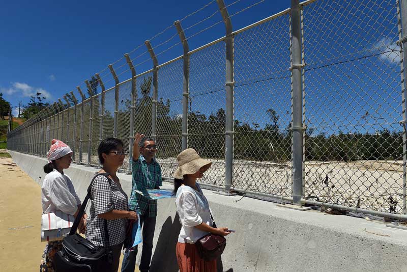 Hiroyuki Tanaka, a protestor against the expansion of the Marine base at Camp Schwab in Henoko, teaches visitors from Ie Shima, an island to the north of Okinawa, what the construction of two airstrips in Oura Bay will do to the ecology of the area, which is home to many species of coral, fish, and the dugong. The fence is the separation between Henoko and the base. (Tiffany Tompkins-Condie, McClatchy.)