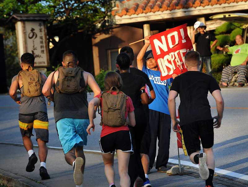 A group of Marines on an early morning run pass a protestor standing outside the gates of Marine Corps Air Station Futenma in Ginowan, Okinawa, Japan, on July 30, 2015. Protestors' presence have become the norm, as residents are afraid of air crashes and are tired of the military base in the center of their city. (Tiffany Tompkins-Condie, McClatchy.)